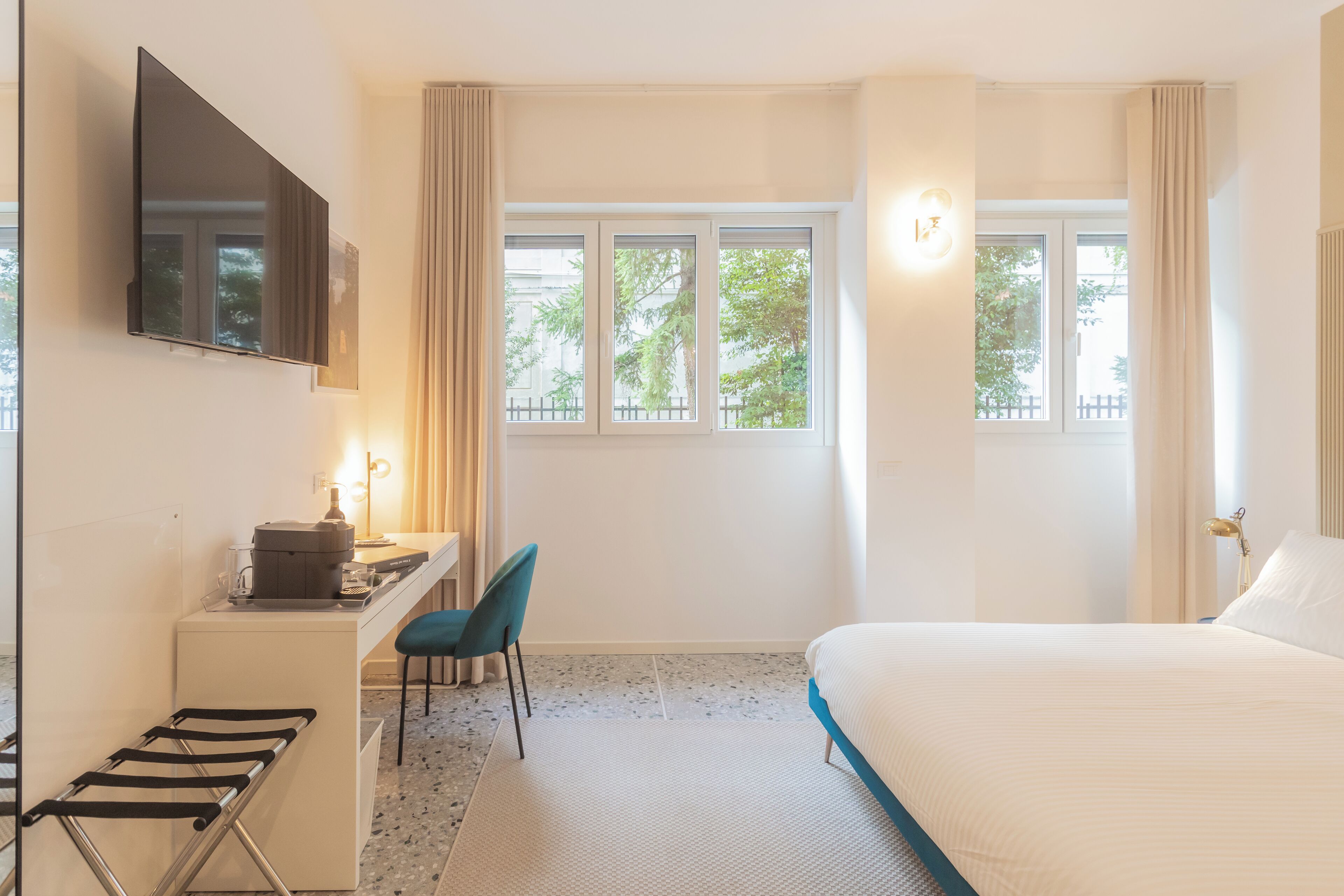 Une chambre d’hôtel comprenant un lit, un bureau avec une chaise, un téléviseur fixé au mur et une fenêtre avec des rideaux.