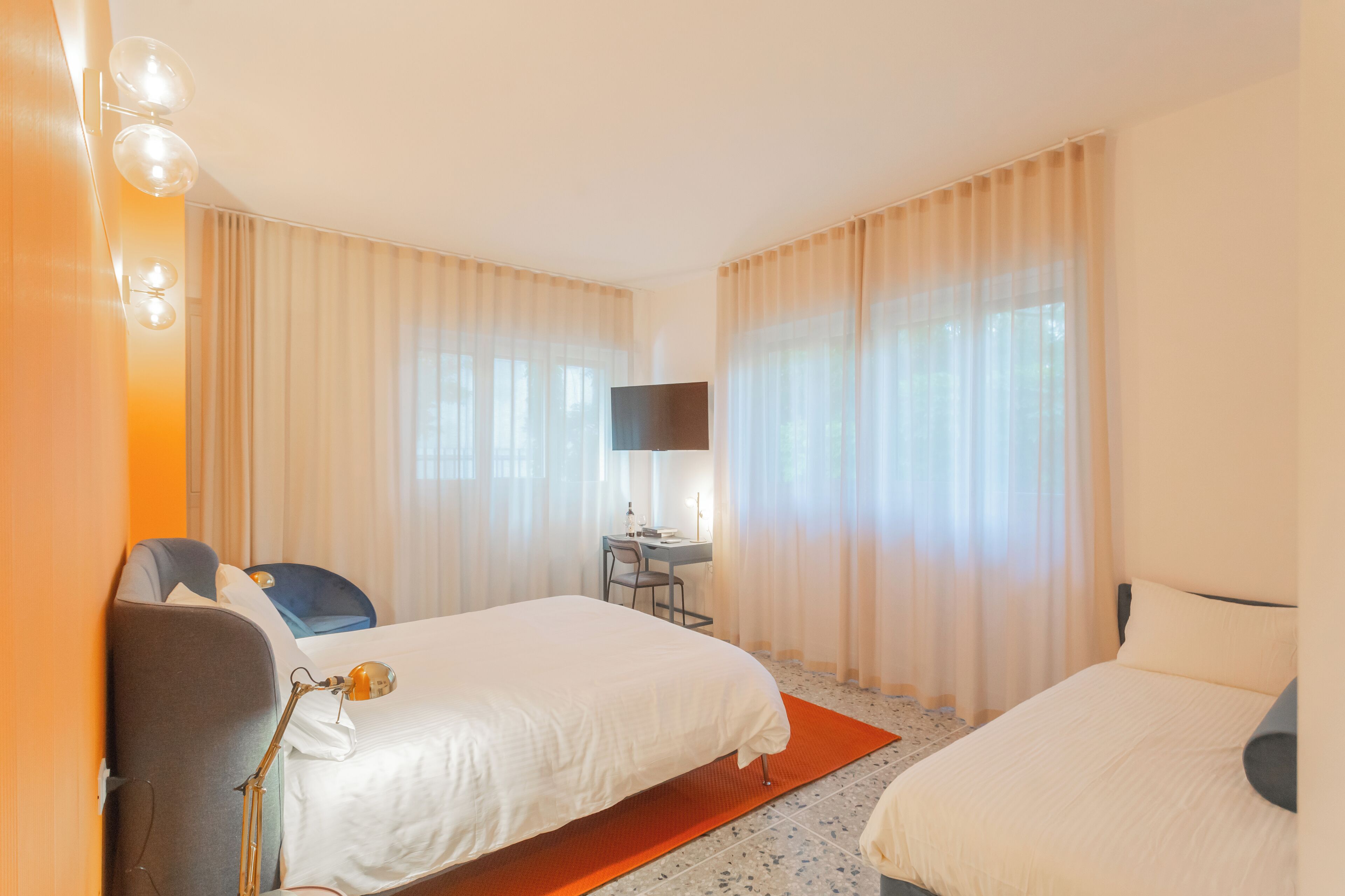 A hotel room with two beds, a desk, a chair, a TV, and curtains.