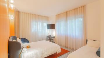 A hotel room with two beds, a desk, a chair, a TV, and curtains.