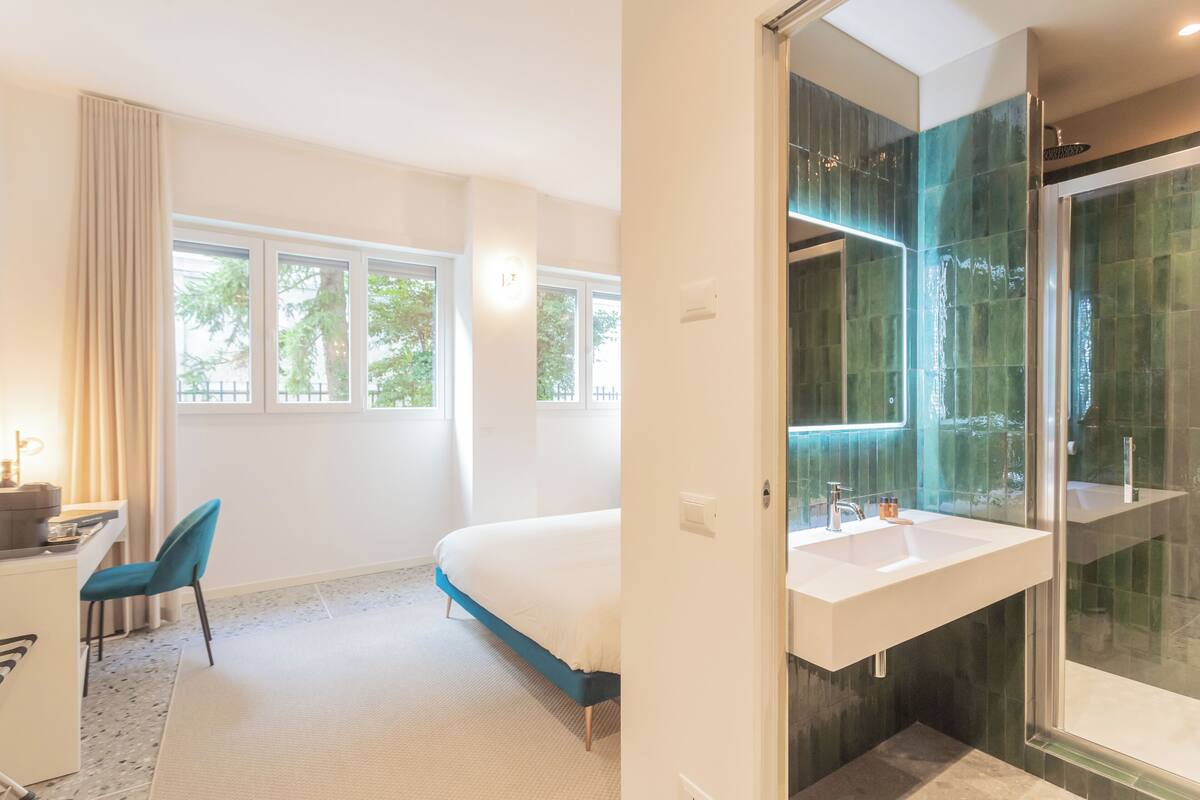 Une chambre moderne avec un grand lit, un bureau avec une chaise et une salle de bain dotée d’une douche en verre.
