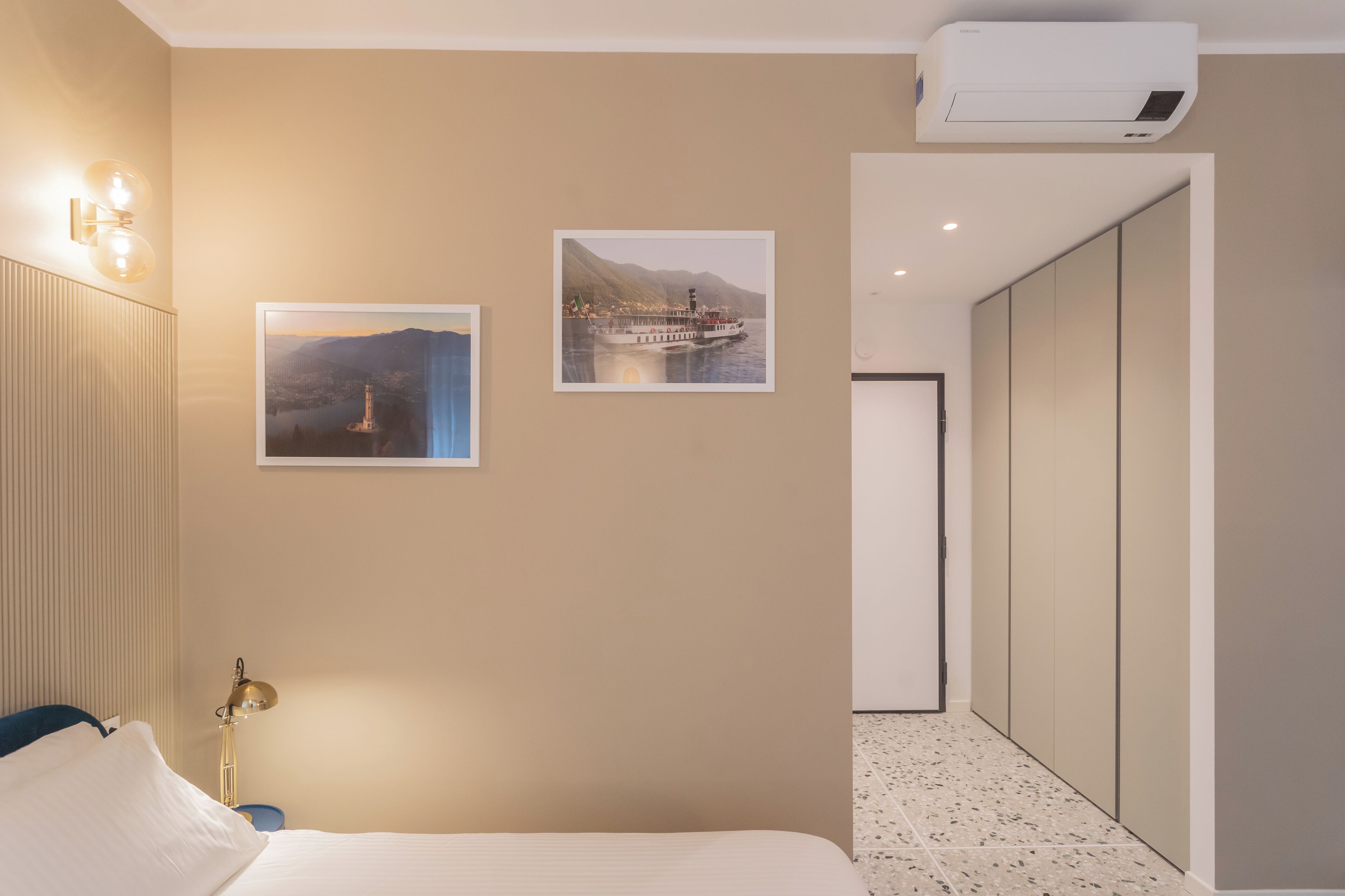 Una camera d'albergo con un letto, opere d'arte a parete, una lampada, un condizionatore d'aria e un armadio.