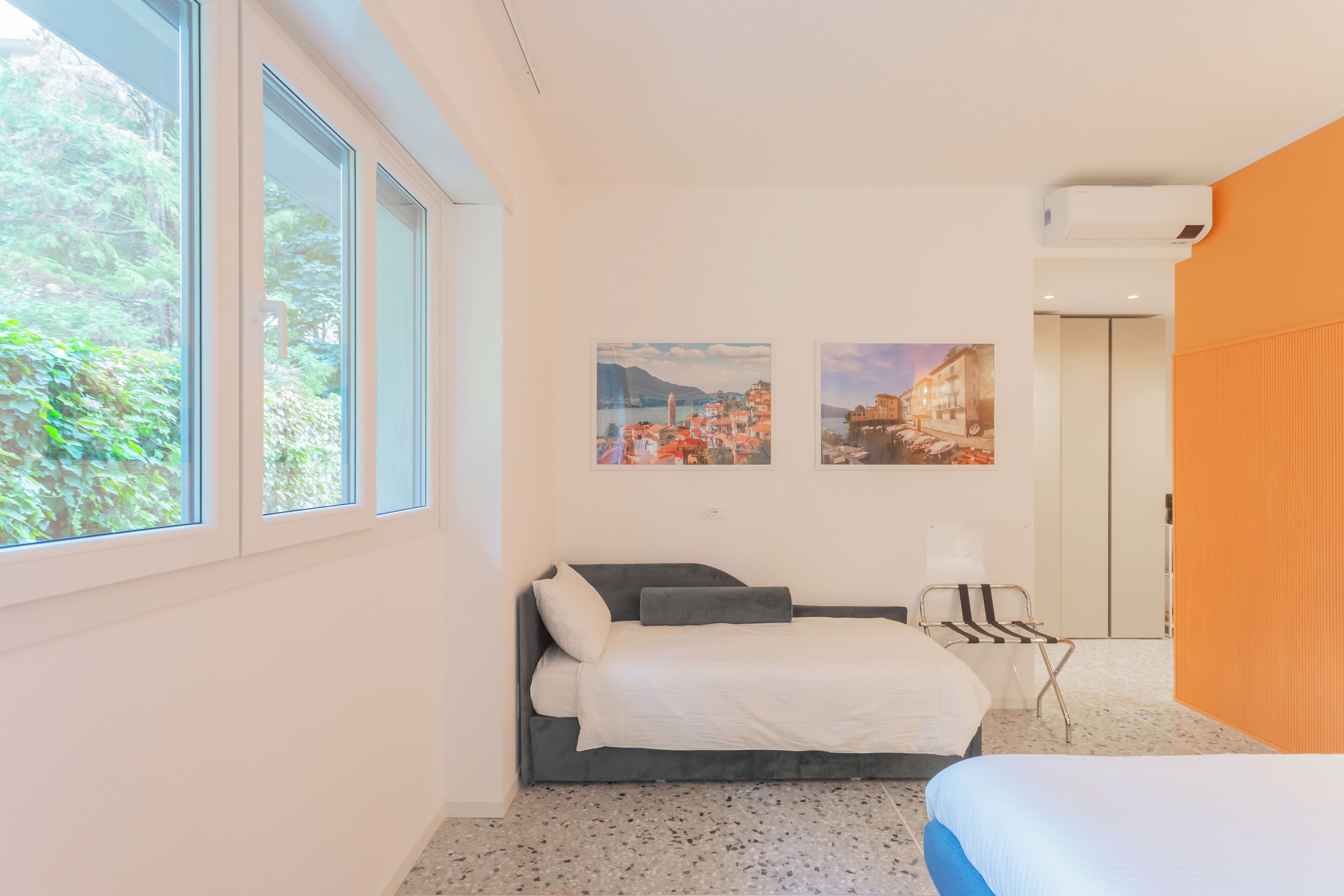 A modern hotel room with a bed, a chair, and two paintings on the wall.