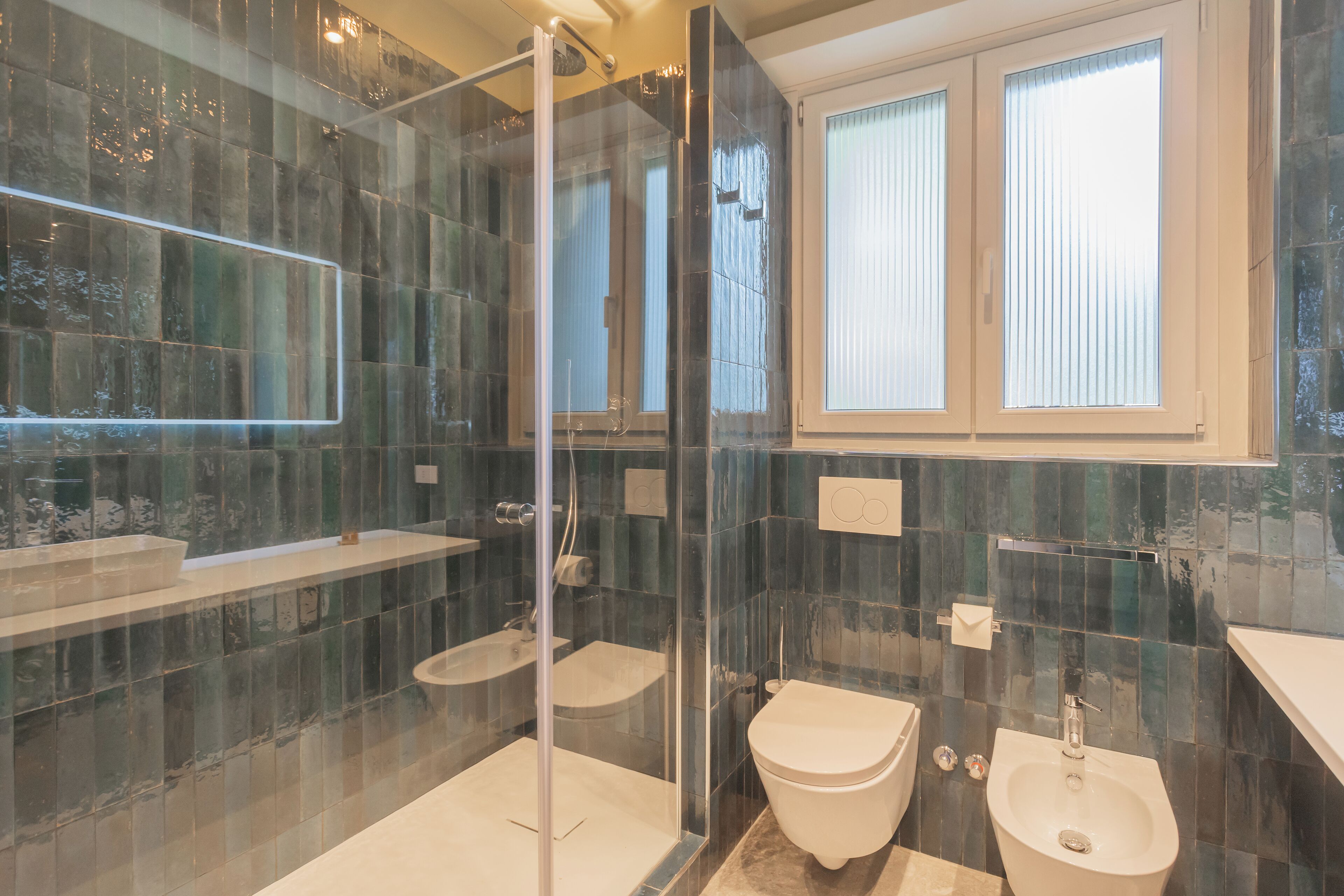A modern bathroom with a glass-enclosed shower, a toilet, and a bidet.