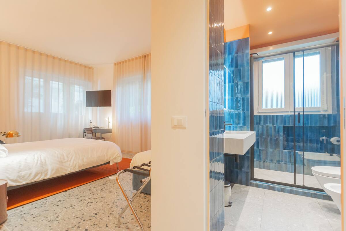 Une chambre d’hôtel comprenant un lit, un bureau, une chaise, une télévision et une salle de bain avec une douche à parois de verre.