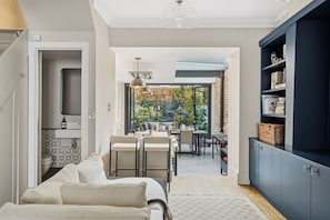 Un salon moderne avec un canapé, un coin repas avec des chaises, une cuisine équipée d’armoires et une vue sur l’extérieur.