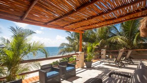 A covered outdoor seating area with wicker furniture, a view of the ocean, and palm trees. - Casa Del Sol: Beachfront Villa, Infinity Pool, 7 bedrooms, Made for Big Groups (Puerto Morelos)