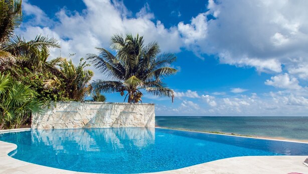 A clear blue pool with a stone wall and palm trees, overlooking the ocean. - Casa Del Sol: Beachfront Villa, Infinity Pool, 7 bedrooms, Made for Big Groups (Puerto Morelos)