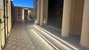 A paved pathway leading to a building entrance with columns and a large door.