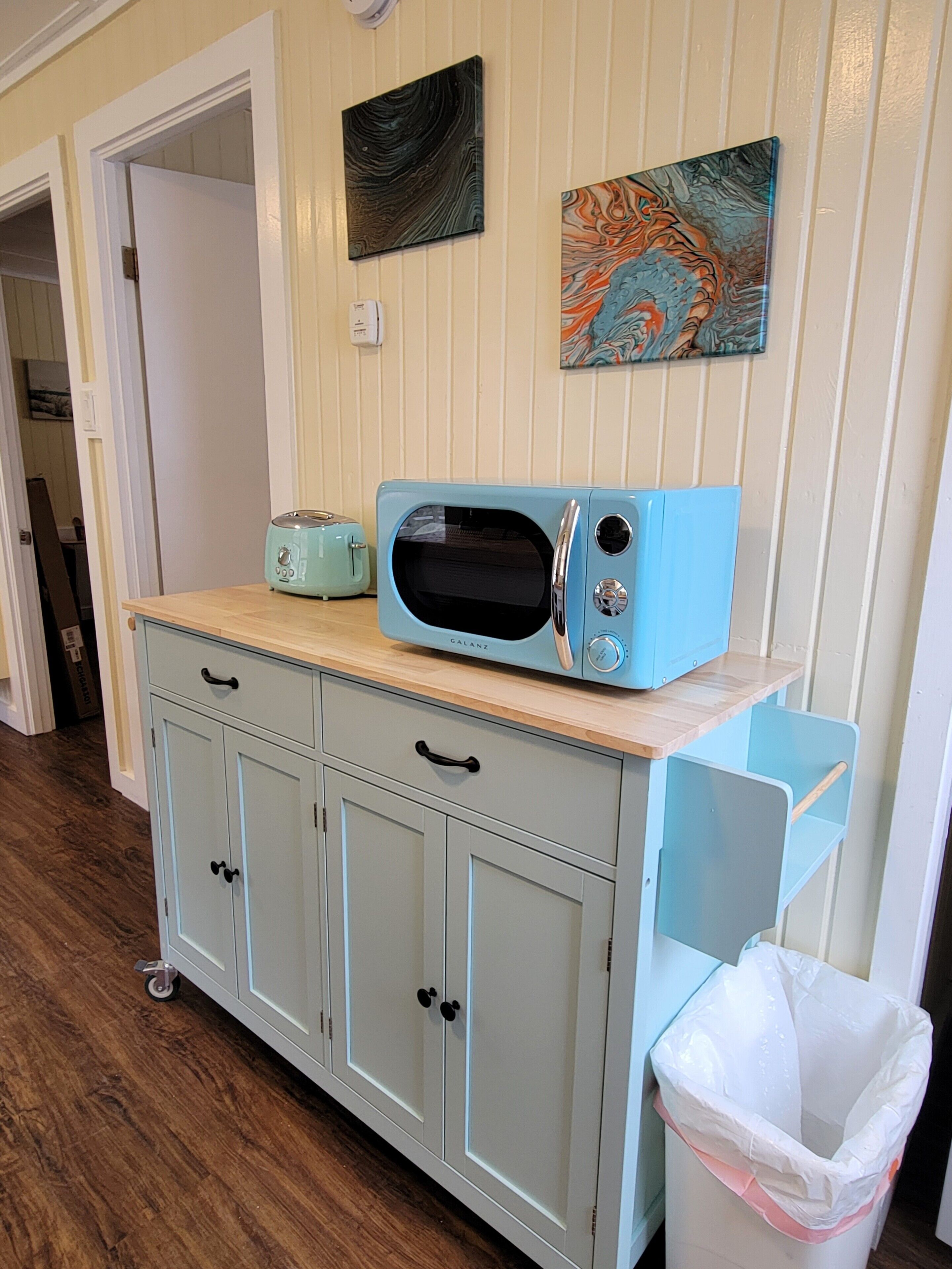 Une petite cuisine équipée d’un micro-ondes bleu, d’un grille-pain et d’une poubelle.