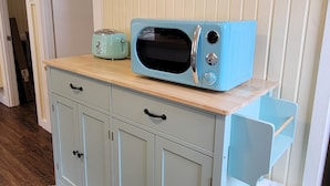 A kitchenette with a blue microwave, a toaster, and a trash can.