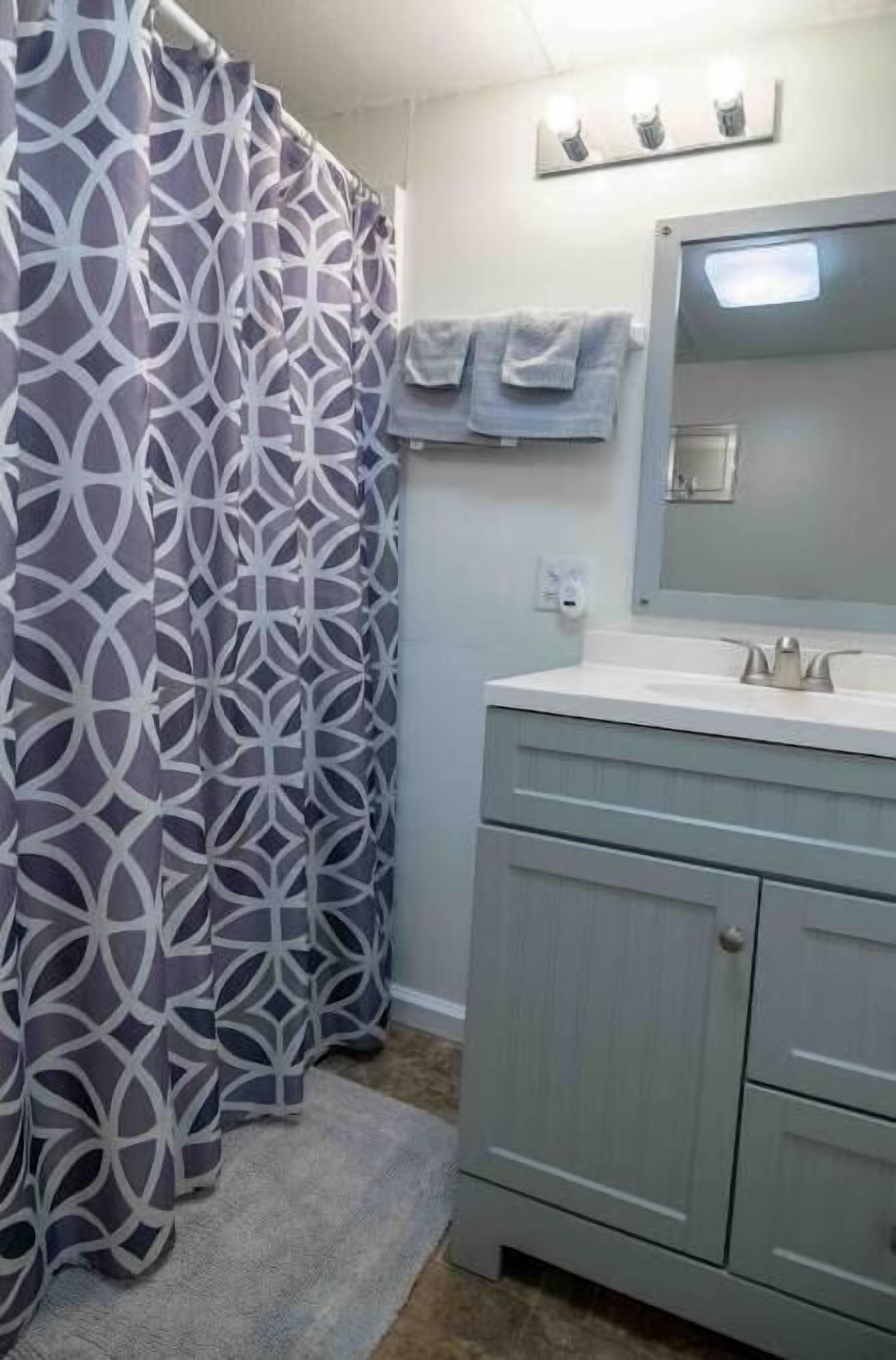A bathroom with a patterned shower curtain, a sink with a mirror, and a towel rack.