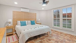 Une chambre à coucher avec un lit, des tables de chevet, un ventilateur de plafond et une fenêtre avec des stores.