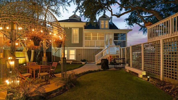 Une maison à deux étages avec une pelouse bien entretenue, un espace extérieur aménagé avec des guirlandes lumineuses et un jardin clôturé.