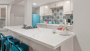 Une cuisine moderne avec des meubles blancs, un réfrigérateur bleu et un plan de travail en marbre.