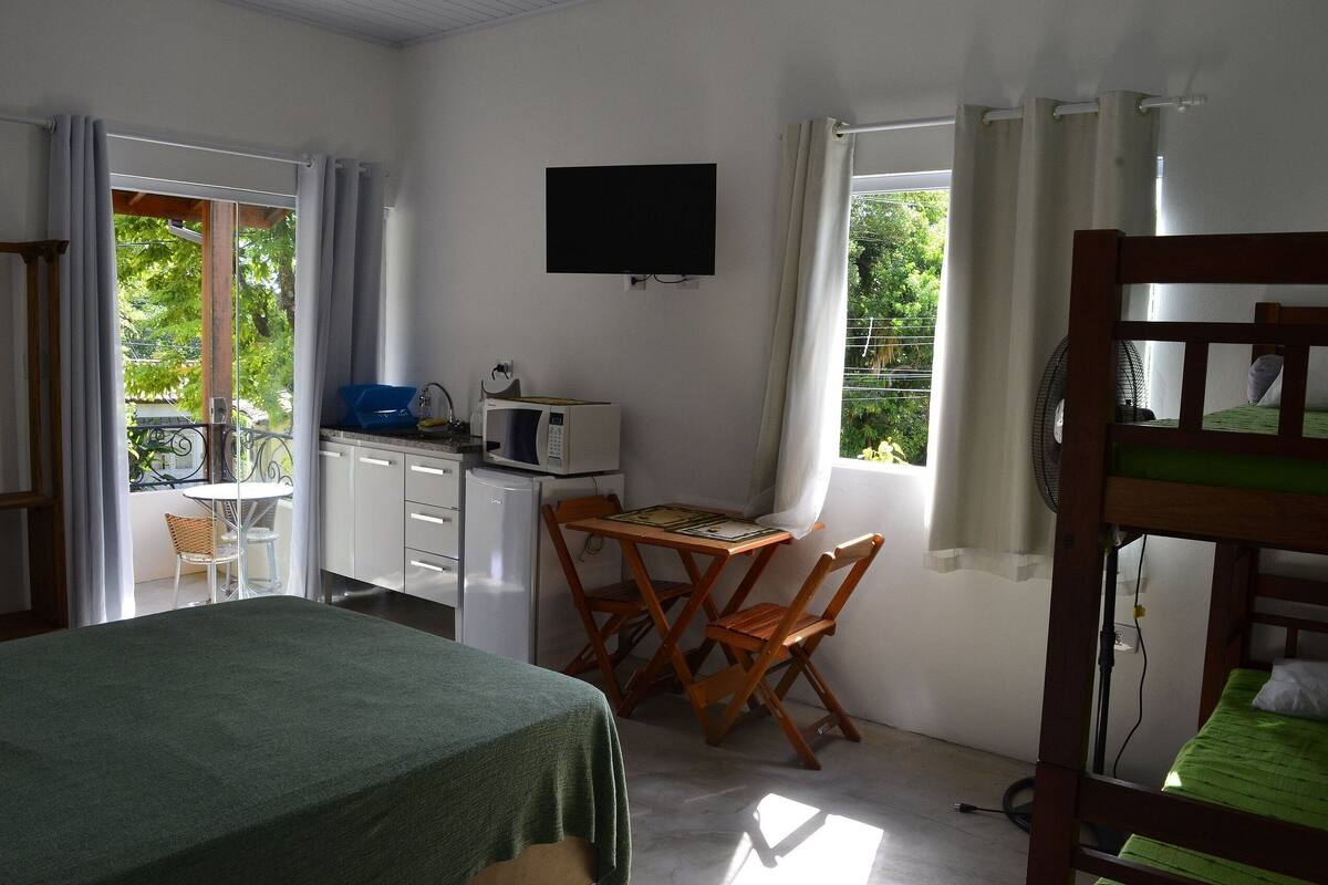 A room with a bed, a desk with a chair, a TV on the wall, and a window with curtains.