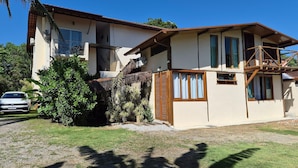 A two-story house with a balcony, a car parked in the driveway, and a well-maintained lawn. - Suites Paquetá Ilhabela (Ilhabela)
