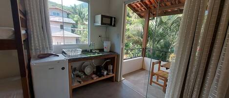 Cocina compacta con microondas, fregadero y refrigerador pequeño. Balcón con una silla y vista a zonas verdes.