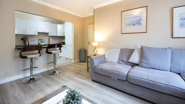 A living room with a grey sofa, two bar stools, a small table with a plant, and a kitchen in the background. - Fantastic 2BD apt in THE best location in Dublin (Dublin)