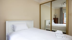 A neatly made bed with white linens and a folded towel, a large mirror, and a window with curtains. - Fantastic 2BD apt in THE best location in Dublin (Dublin)