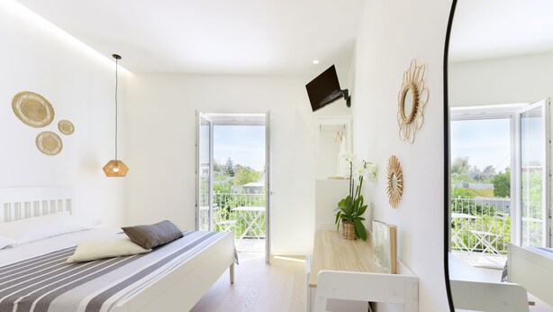 A bright bedroom with a bed, bedside table, and a view of the outdoors. - Sea More - Rooms (Procida)