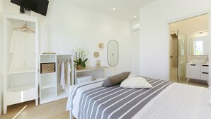 A bedroom with a bed, a wardrobe, a TV, a mirror, and a bathroom visible through an open door. - Sea More - Rooms (Procida)
