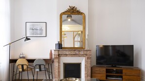 Un salon avec une cheminée, un téléviseur, un bureau avec des chaises et un tableau encadré au mur.