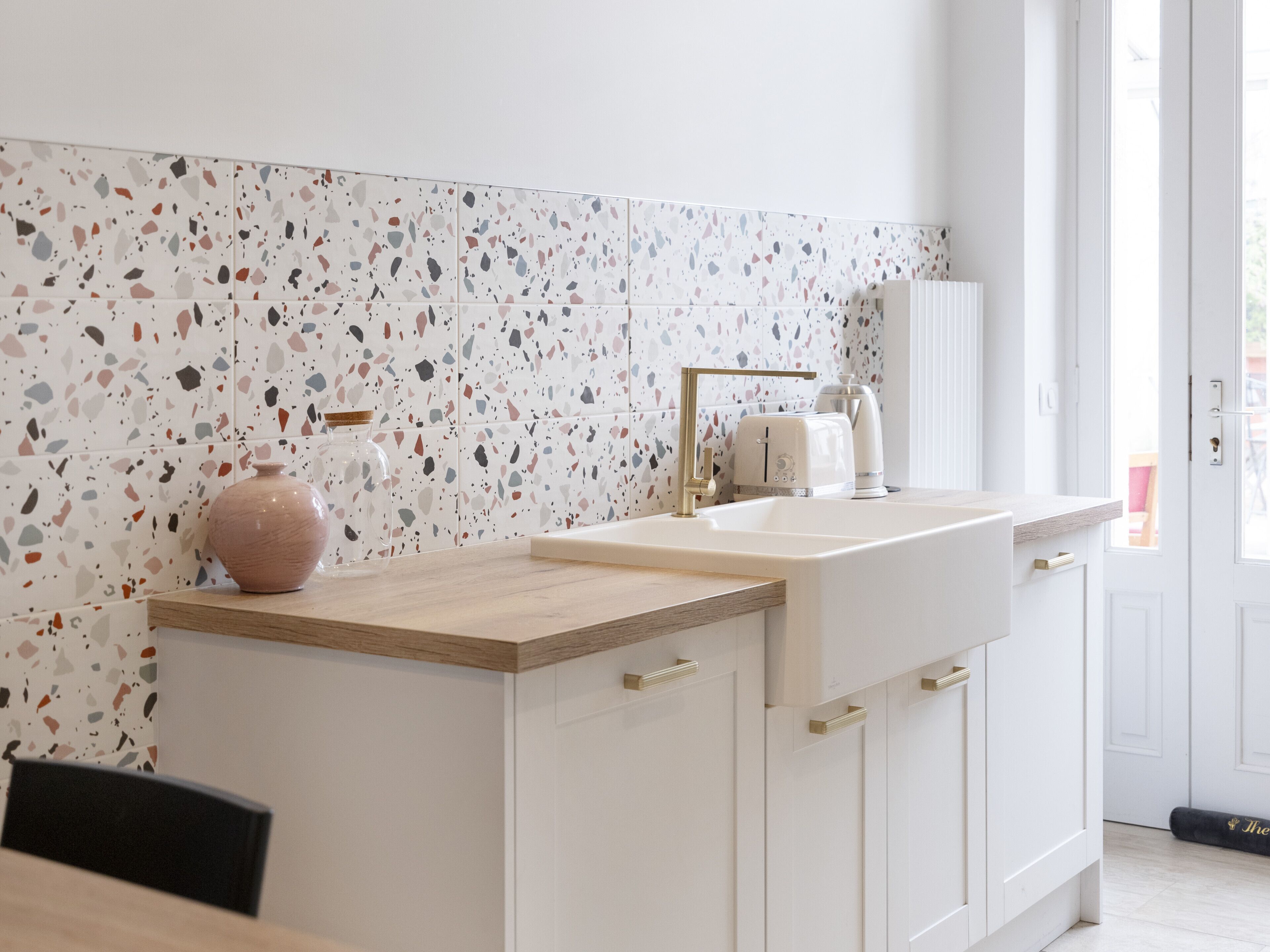 Eine moderne Küche mit weißer Arbeitsplatte, einer rosa Vase, einem weißen Spülbecken und einer Spritzschutzwand mit bunten Tupfen.