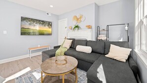 A modern living room with a grey sofa, a round coffee table, and a large landscape painting on the wall. - Cozy Apt in Center City Very Central Location (Philadelphia)