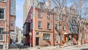 A row of brick buildings with a 'ONE WAY' street sign, a clear sky, and leafless trees. - Cozy Apt in Center City Very Central Location (Philadelphia)