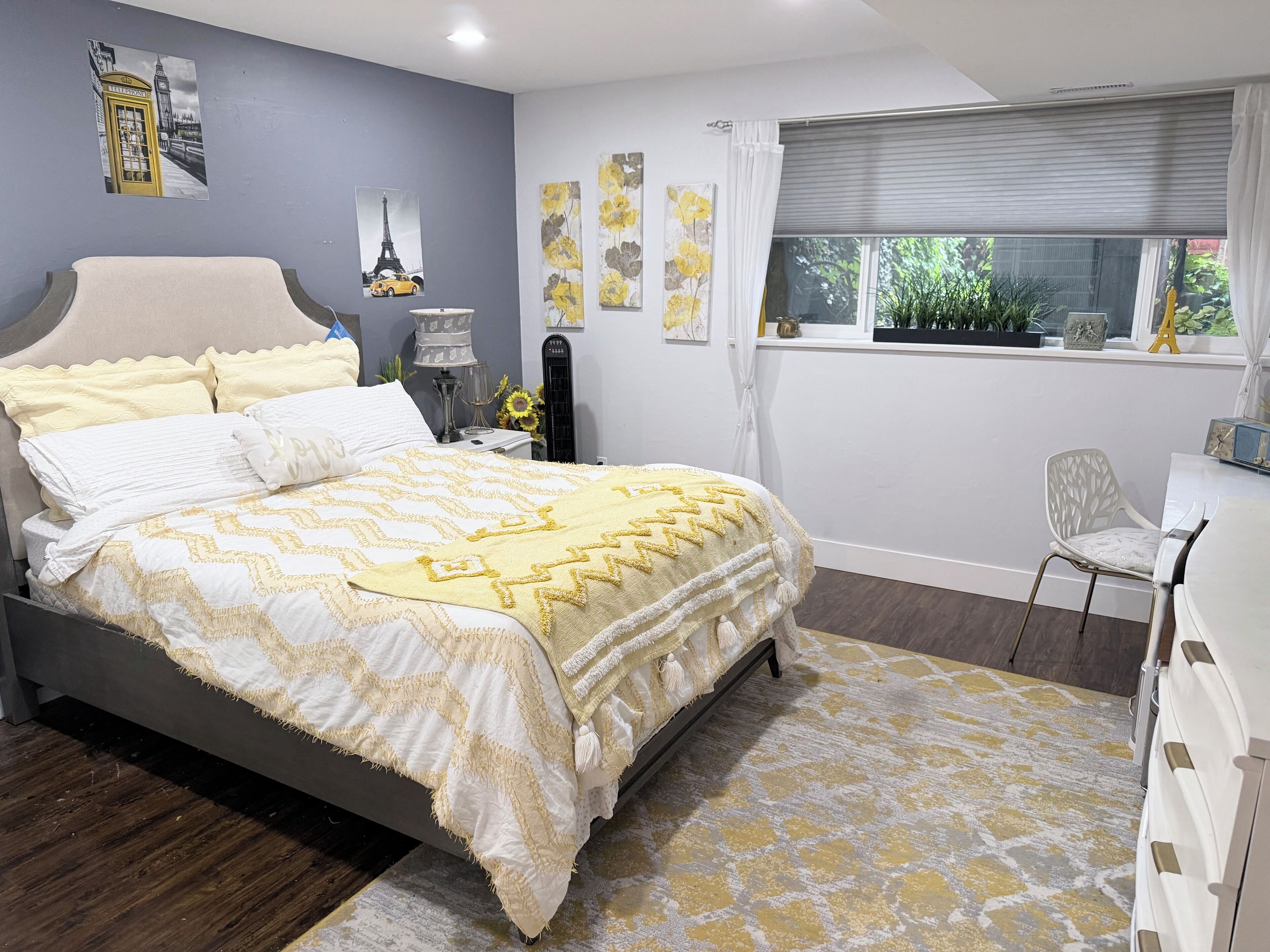 A bedroom with a bed, a desk, a chair, and artwork on the walls.