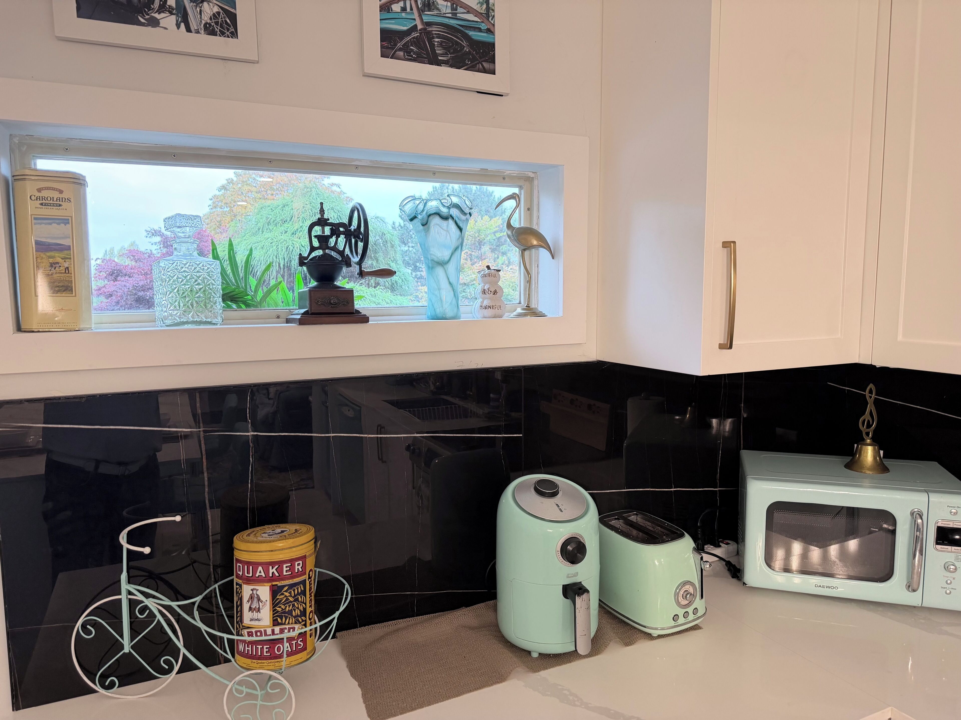 Una cocina con encimera negra, un tostador vintage, un microondas moderno y una ventana con vistas a zonas verdes.