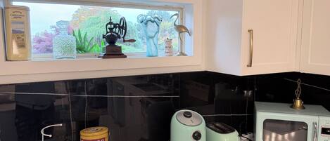 Una cocina con encimera negra, un tostador vintage, un microondas moderno y una ventana con vistas a zonas verdes.