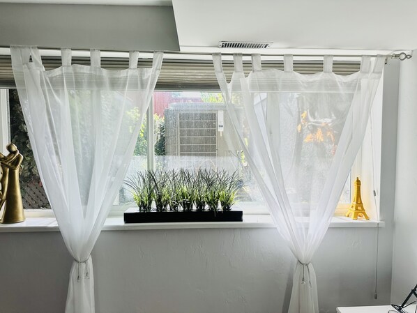 A window with sheer white curtains, a small potted plant, and a golden Eiffel Tower model on the windowsill.