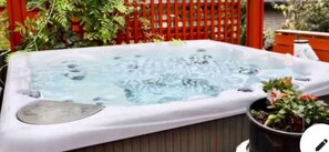 A hot tub with a wooden deck, surrounded by plants and a red fence. - Newer Fifties theme large 2 bdrm, hot tub and golf green! Entire ground floor. (Delta)