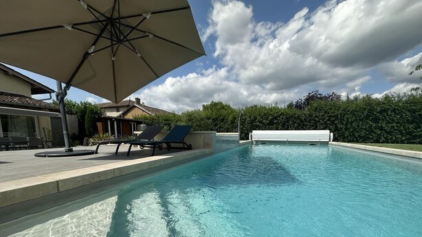 Una piscina con zona de descanso, que incluye una sombrilla y sillas reclinables.