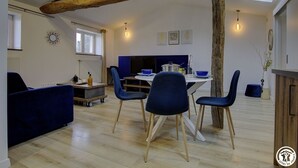 Una sala de estar moderna con comedor, que incluye una viga de techo de madera, un sofá, una mesa de comedor con sillas y una zona de cocina con televisor y armarios.