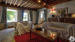 Ein gemütliches Zimmer mit Holzbalkendecke, zwei abgedeckten Stühlen, einem Sofa, einem Holztisch und einem roten Teppich.