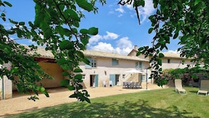 Ein zweistöckiges Haus mit einer Terrasse, Sitzgelegenheiten im Freien und einem gepflegten Rasen.