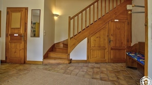 Eine Holztreppe führt zu einer zweiten Etage, eine Holztür, ein Spiegel und eine Bank mit einem farbenfrohen Kissen.