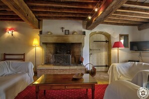 A cozy room with a fireplace, two white upholstered chairs, a wooden table, and a red patterned rug. - La Caronnière - Peyzieux-sur-saone (PEYZIEUX-SUR-SAONE)