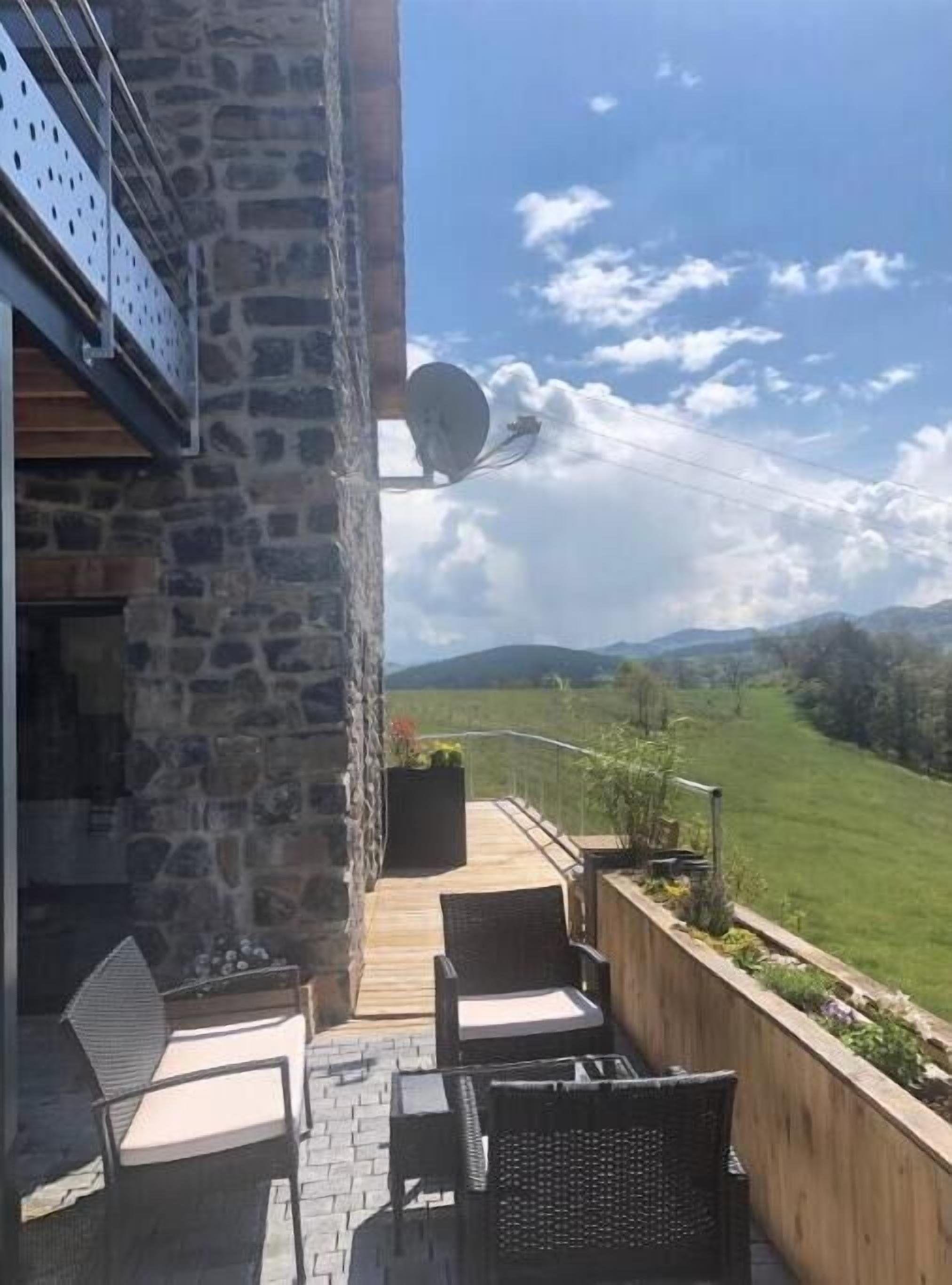 Un balcon aménagé avec du mobilier d’extérieur, un mur en pierre et une vue sur un paysage verdoyant et des montagnes.