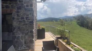 A balcony with outdoor furniture, a stone wall, and a view of a green landscape and mountains.