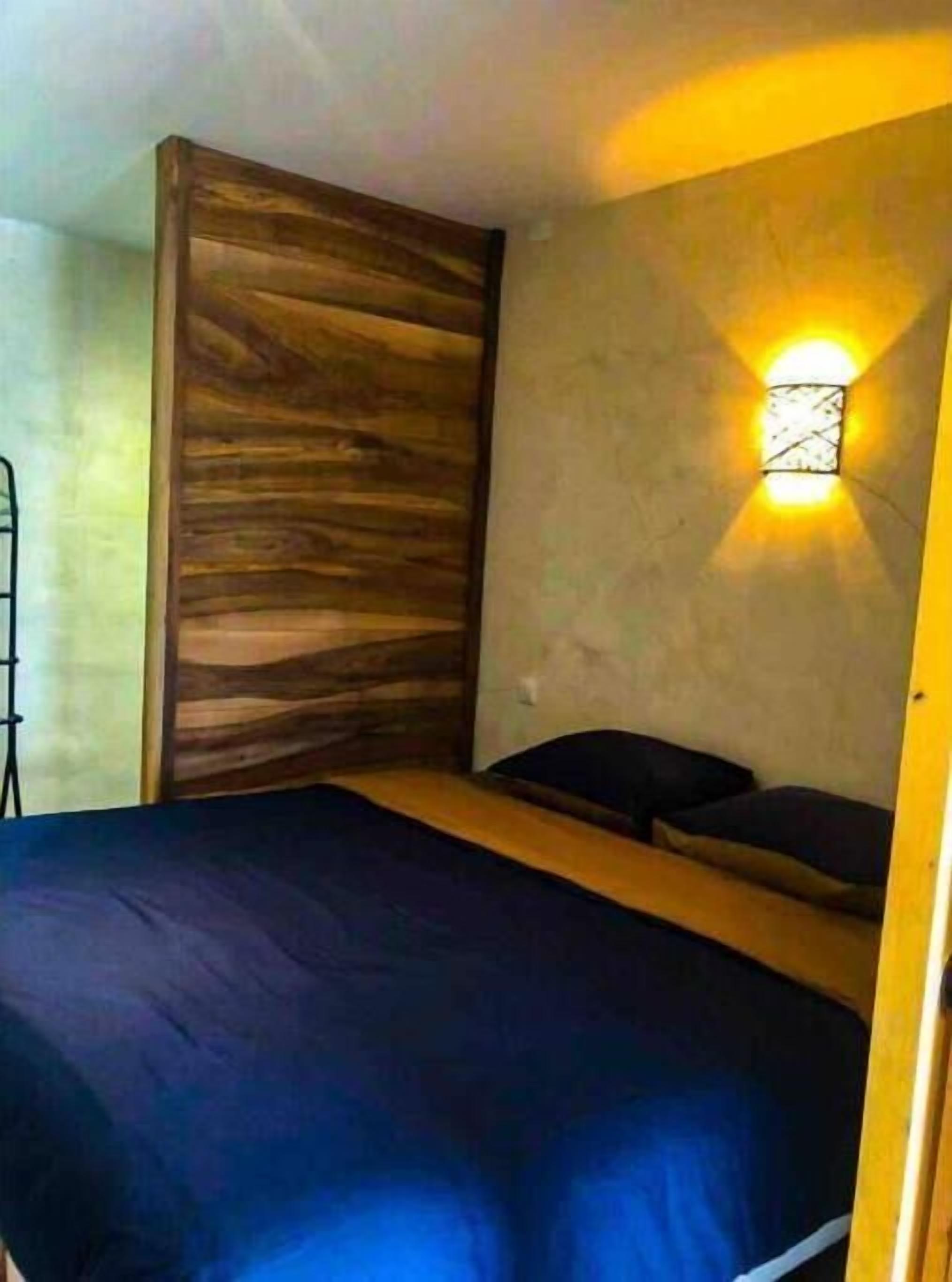 A bedroom with a wooden headboard, a bed with a dark blue bedspread, and a wall-mounted light fixture.