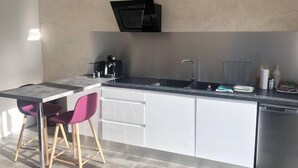 Une cuisine moderne dotée d’un îlot central, de meubles blancs, d’une hotte noire et d’un évier en acier inoxydable.