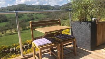 Une terrasse en bois avec un banc et une table, offrant une vue panoramique sur un paysage vallonné et un ciel dégagé.