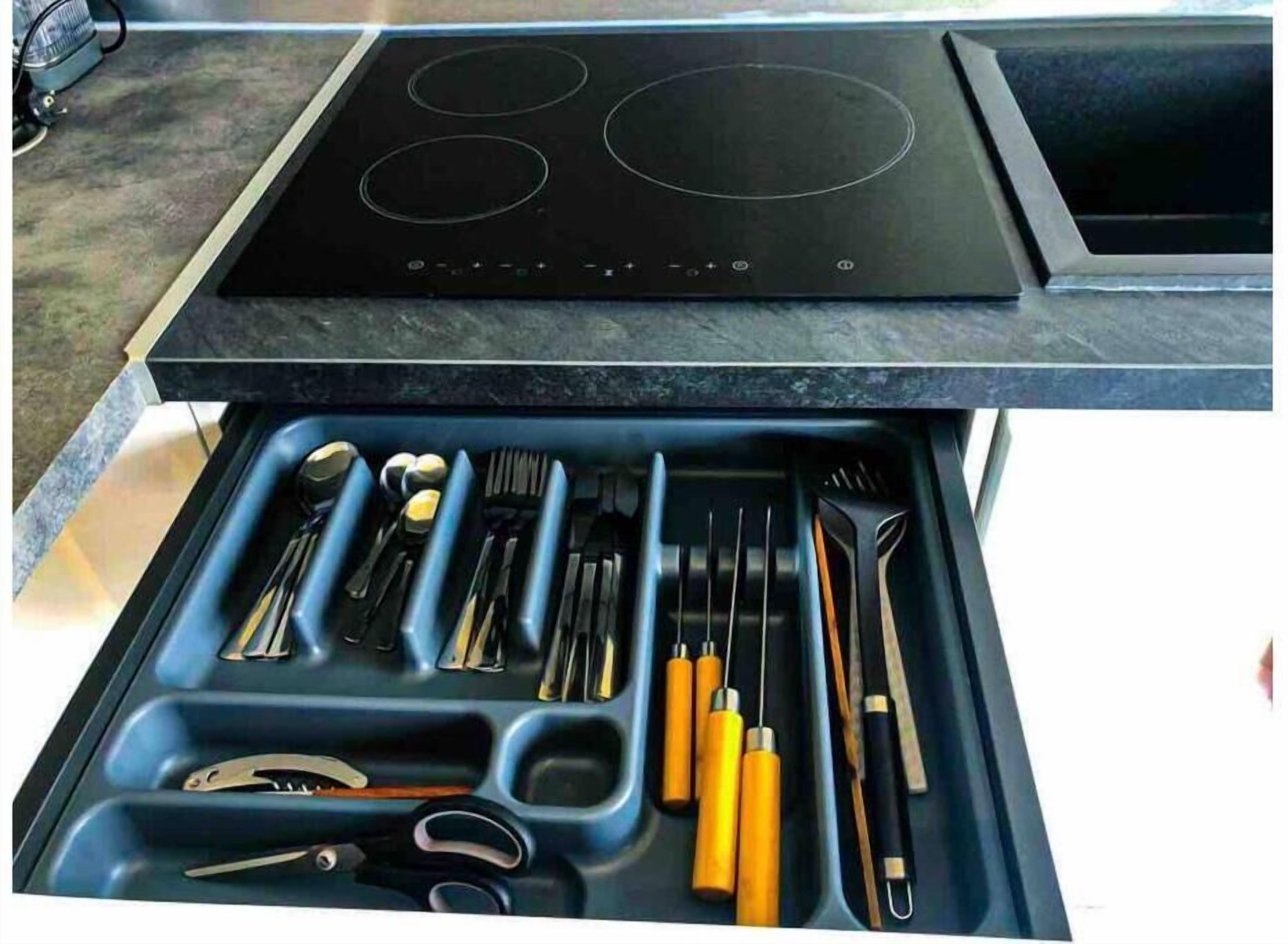 A kitchen with a black stovetop and a drawer below containing various utensils.