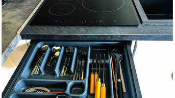A kitchen with a black stovetop and a drawer below containing various utensils.