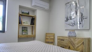 Une chambre à coucher comprenant un lit, une table de chevet en bois, une bibliothèque et un climatiseur fixé au mur.