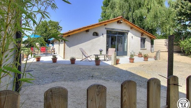 Un petit bâtiment d’un seul étage, doté d’un toit en tuiles, entouré de plantes en pot et bordé d’une allée en gravier.