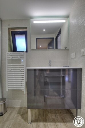 Une salle de bain moderne avec un lavabo en acier inoxydable, un miroir au-dessus et un porte-serviettes fixé au mur.
